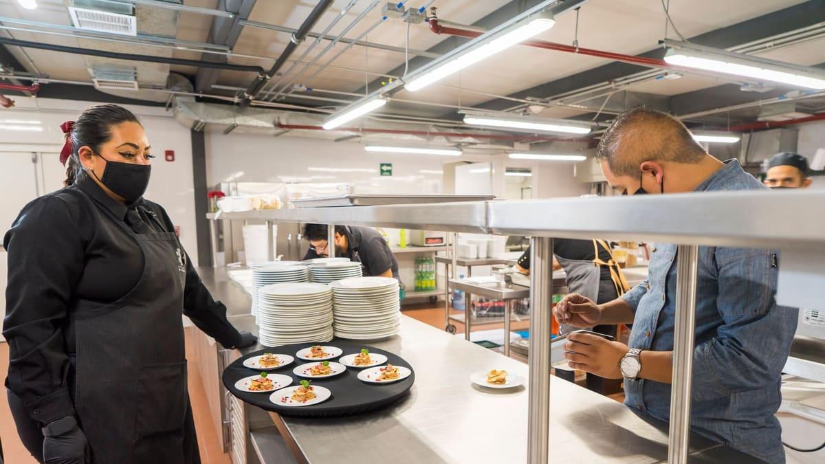 Chef plating a dish on the pass in a busy commercial kitchen